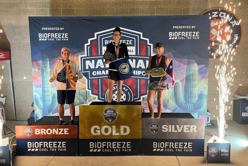Three individuals stand on awards podium.