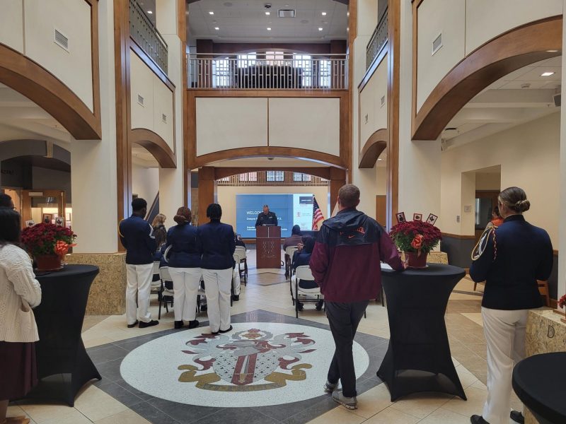 Cadets and other visitors attend the ceremony honoring Lindsay Cherry '58 and his donation of a saber and ring to the Black Cultural Center. Cadets and other visitors stand at high-top tables while a man in a military uniform speaks from a podium.