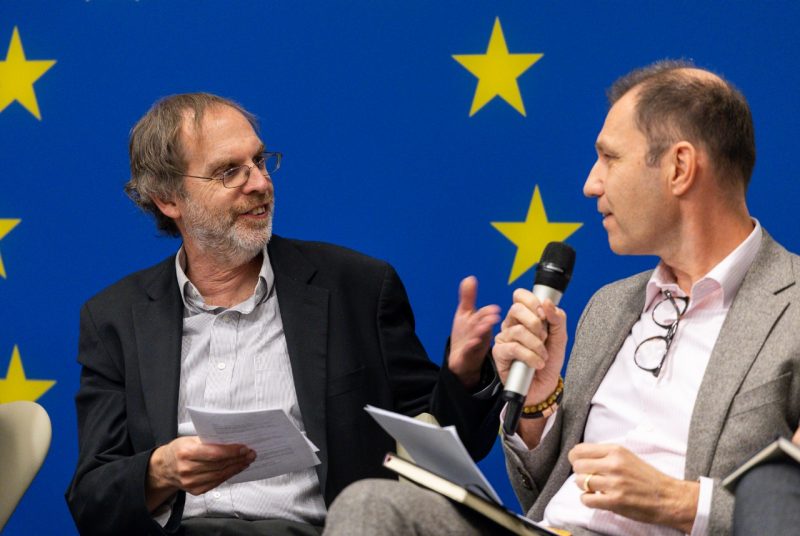 Two men speak during panel discussion. One holds microphone.