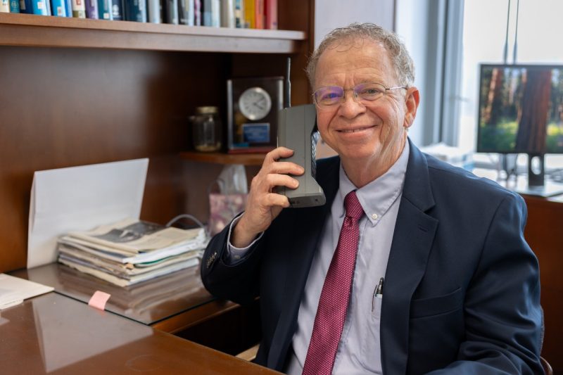Jeff Reed Reed holds up a mobile phone from the 1980s. Photo by Ben Murphy for Virginia Tech.