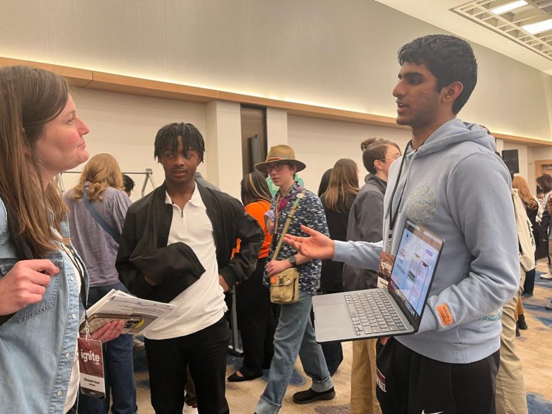 Pranav Kalidindi holds a laptop and speaks to a woman.