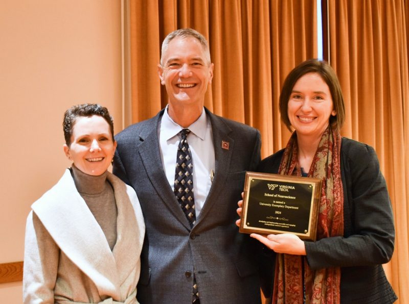 Two neuroscience faculty members pose with the dean of the College of Science while holding a plaque that says, "School of Neuroscience is named a University Exemplary Department 2024."