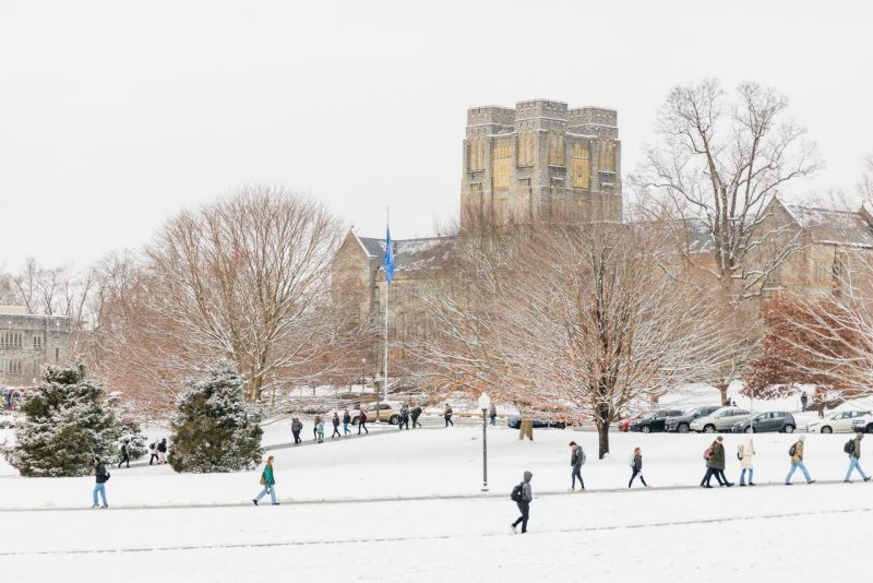 Students, bundled in winter clothes, walk across campus on a snowy day. There is snow on the ground and snow on the branches of trees on the campus lawn.