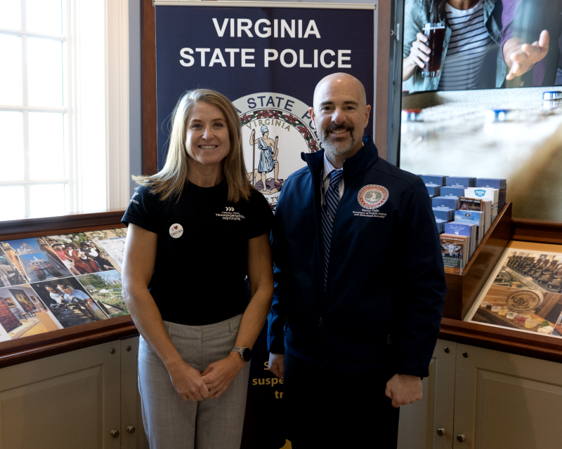 Two individuals stand in front of marketing banners and materials inside a building.