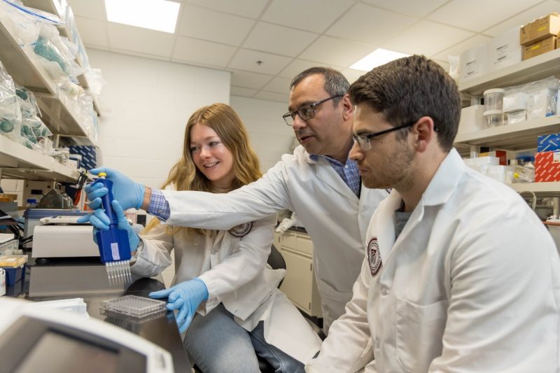 Ramirez Zoetis Roger Ramirez-Barrios (at center) holding a pipette assisting students (at right and left) with their laboratory work