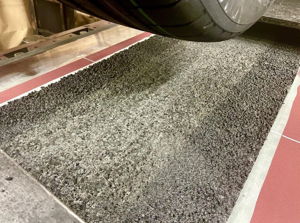 A tire over a testing machine that uses asphalt as the surface