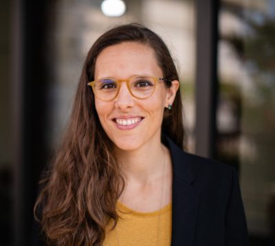 Woman wearing glasses, yellow shirt, and black blazer.