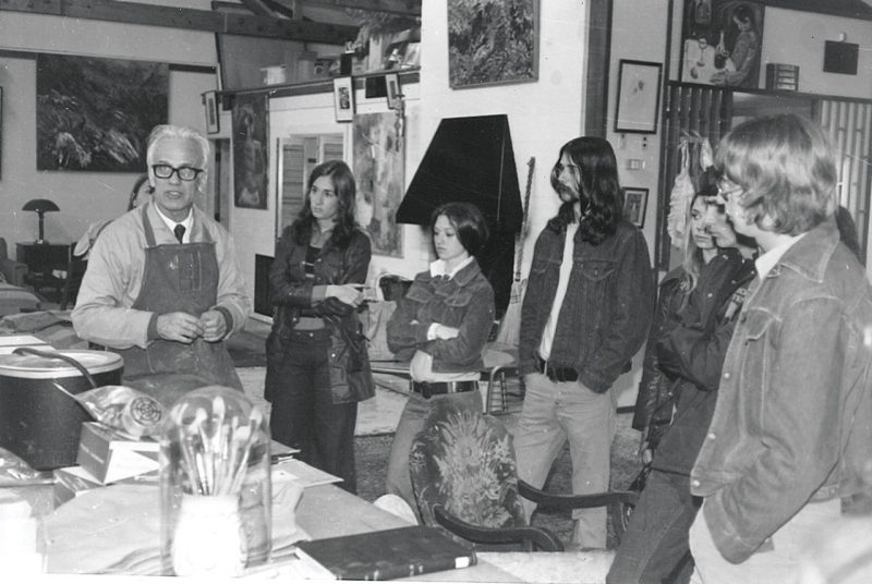 This black and white photo shows a visiting artist, invited to campus by Dean Carter in the 1970s, speaks with Virginia Tech students.