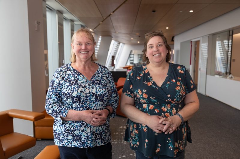 Debbie Bissi and Kristin Sorensen stand in the library space smiling at the camera.