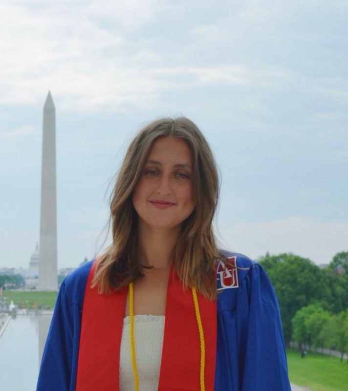 Emma Hare wearing graduation attire standing in front of the Washington Monument