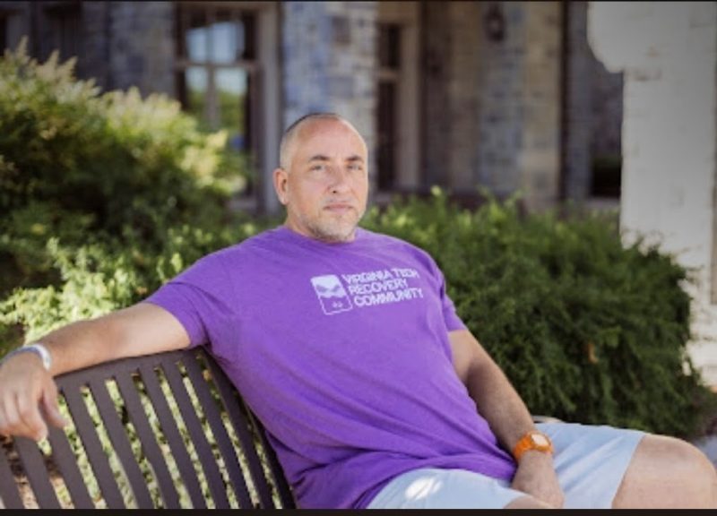 Jon Dance (center) sitting outside on a bench