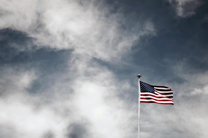 An American flag flying beneath a gray, cloudy sky. Image courtesy Pexels.