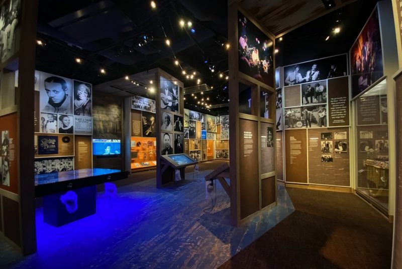 National Museum of African American Music A section of a museum filled with photos, narratives, and glass-front display cases on the walls, and display boards scattered around the space.