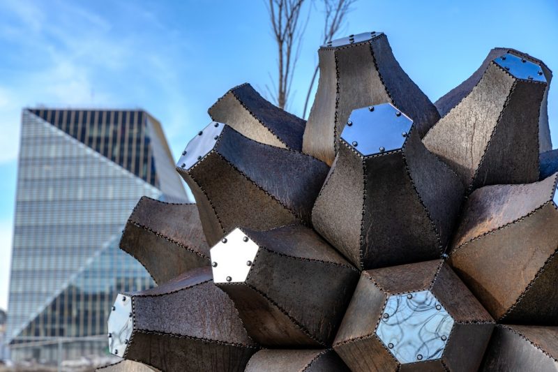 Detail view of Emergence, featuring mirror-finished endcaps, with Virginia Tech’s Academic Building One in the background. Photo by Damon Brewer for Virginia Tech.