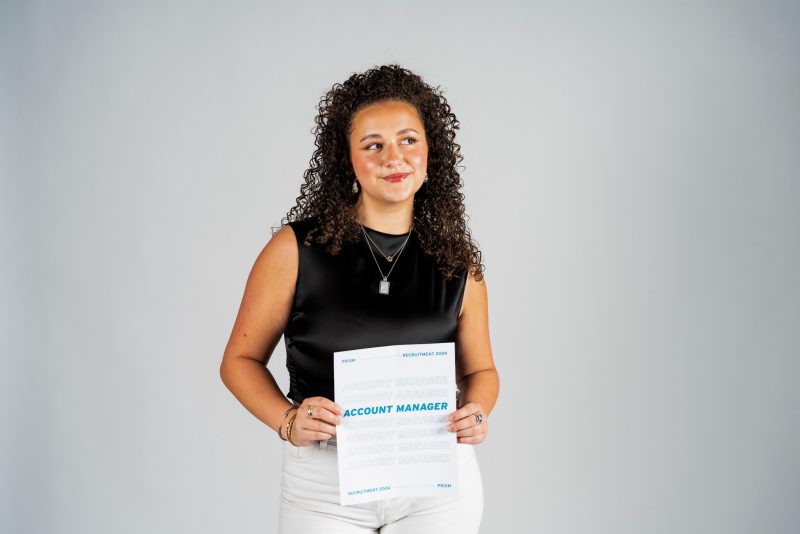Sally Steppling holds a piece of paper announcing her role at PRISM: Account Manager.