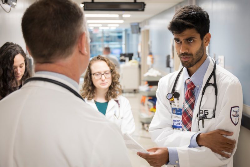 A medical student in a white coat looks intently at a physician in a white coat while on hospital rounds.