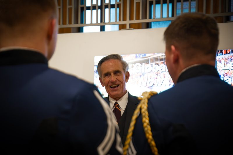 Two cadets face away from the camera toward Rocovich who is smiling and talking to the cadets facing them and the camera.