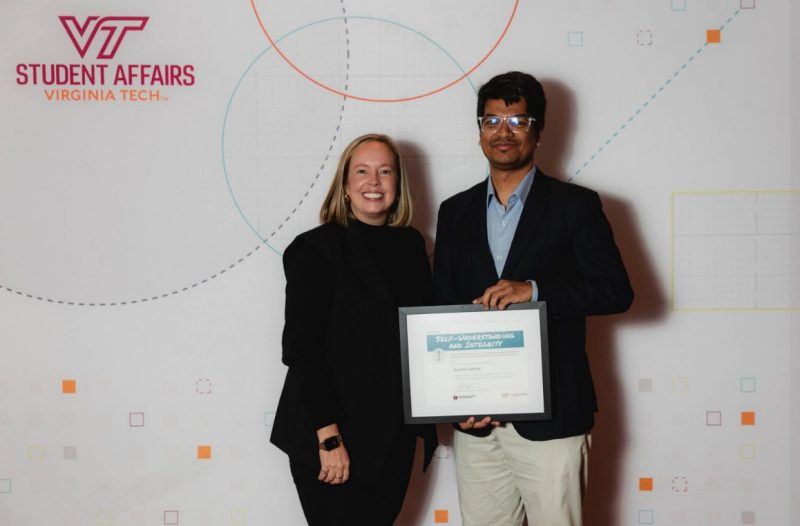 Ibrahim Tahmid and Frances Keene, vice president for Student Affairs, at the Aspire! Awards in December 2024. Photo by Robert Robinson for Virginia Tech. Frances Keene, wearing a black suit and a wrist watch, stands next to Ibrahim Tahmid, wearing a black suit jacket and tan pants. Tahmid is holding an award certificate. The backdrop behind them is white and has a VT Student Affairs logo.