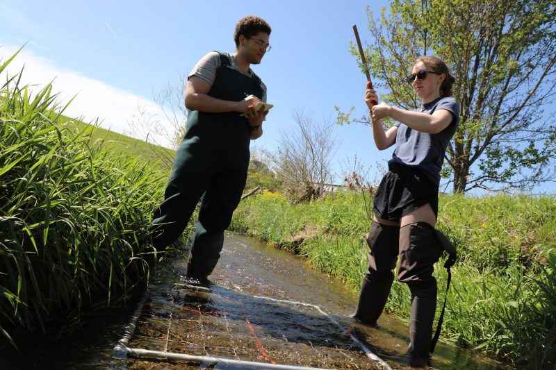 two students stand in a creek collecting measurements