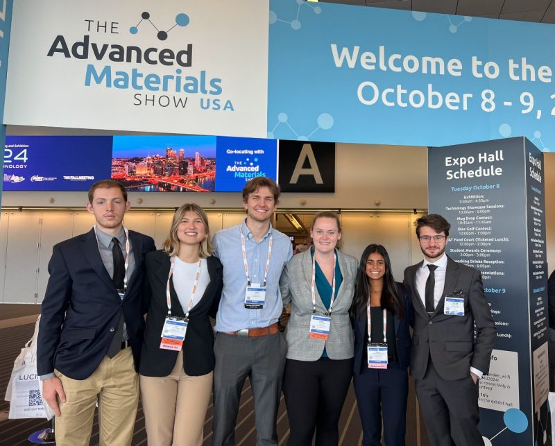 Students pose in front of banner at conference
