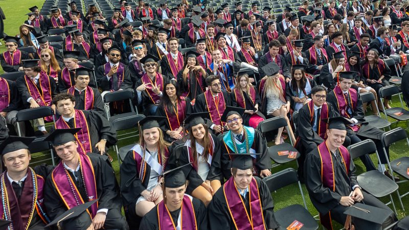 A group of students in black graduation regalia sitting in chairs