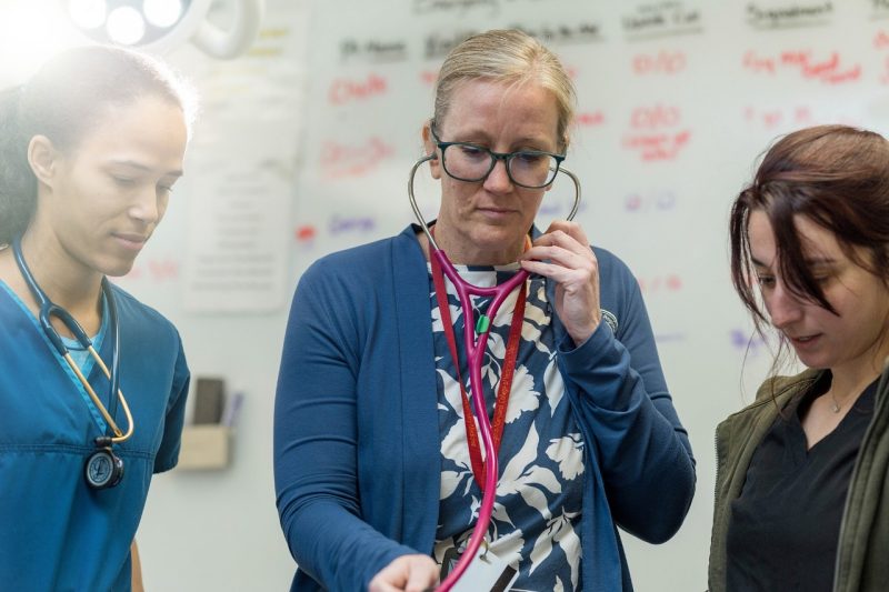 Faculty Awards Bobbi Conner (at center) using a stethoscope on a patient with students at her left and right