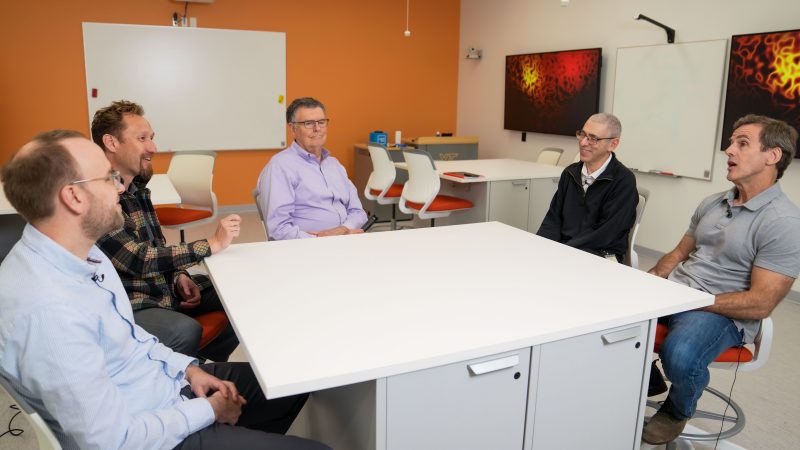Neuroscientists sit around a table discussing major advancements that have taken place over decades.