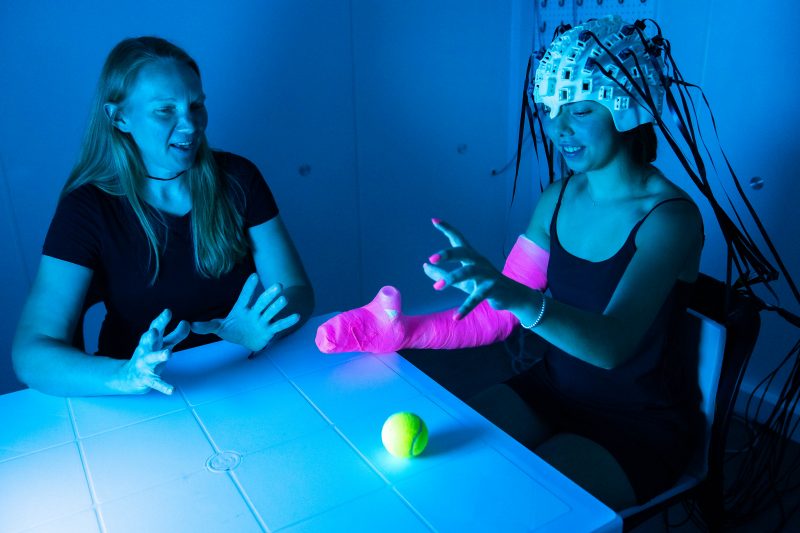 A teen-ager wearing a headset performs mobility exercises while researchers measure magnetic fields in her brain.