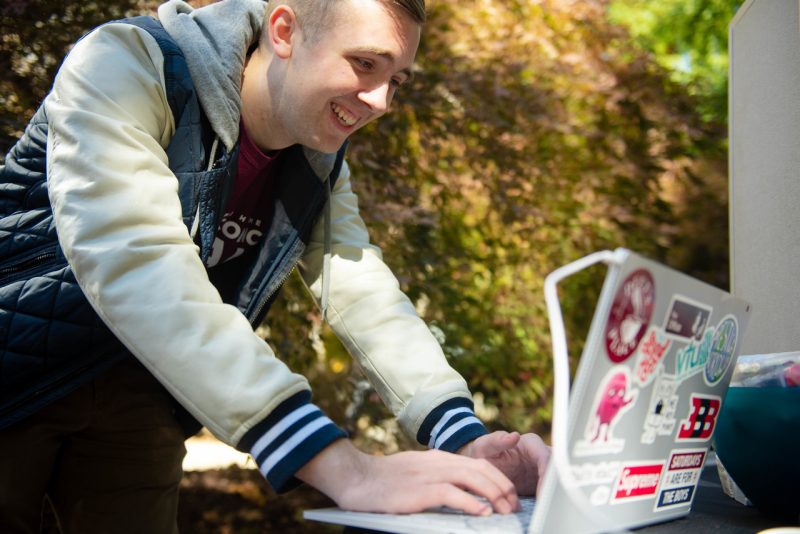 A student smiles while typing on a laptop covered with stickers