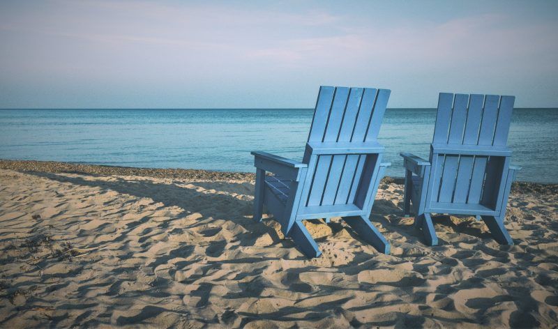 Photo of two blue beach chairs facing the ocean on a beach at sunset.
