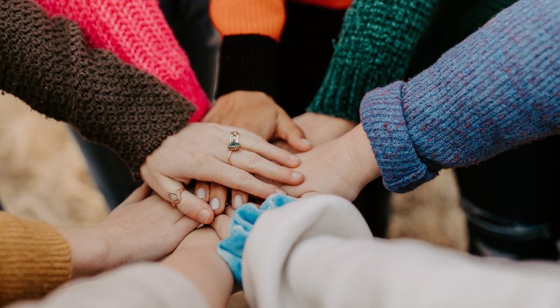 Close-up photo of a circle of people placing their hands atop each others