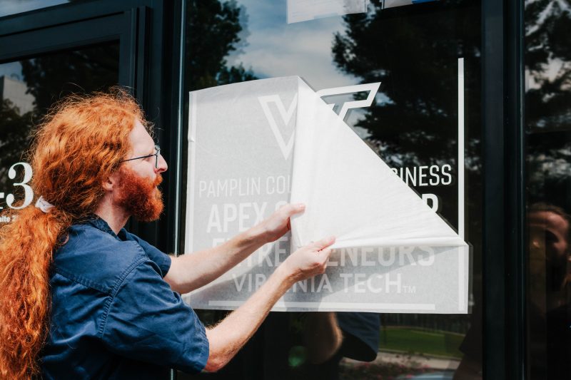 A person peels back adhesive paper on a window to reveal a logo