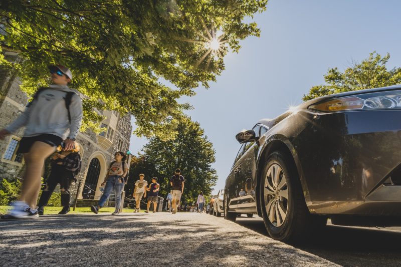 A car is parking on the Blacksburg campus. Students walk by on a sunny day.