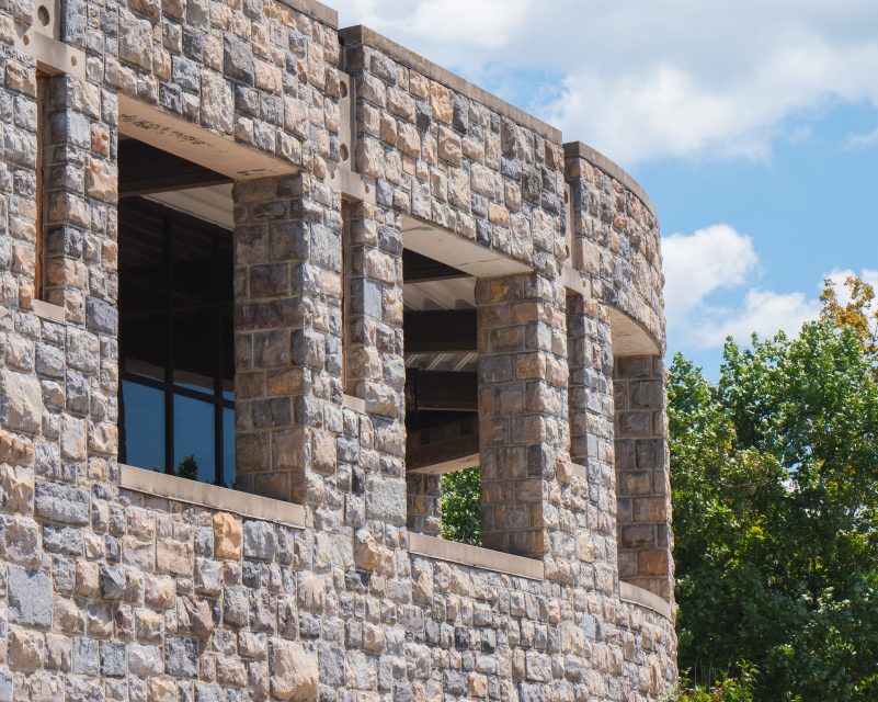 A curved grey Hokie Stone wall with large glass windows on a sunny day