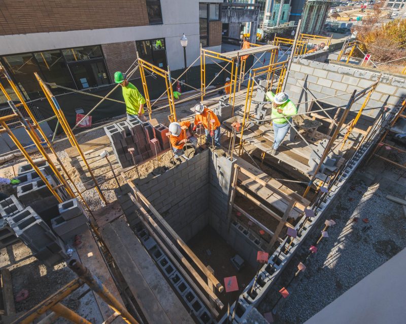 A downward view of construction workers wearing high vis PPE pouring concrete into cement blocks to form an elevator shaft outside