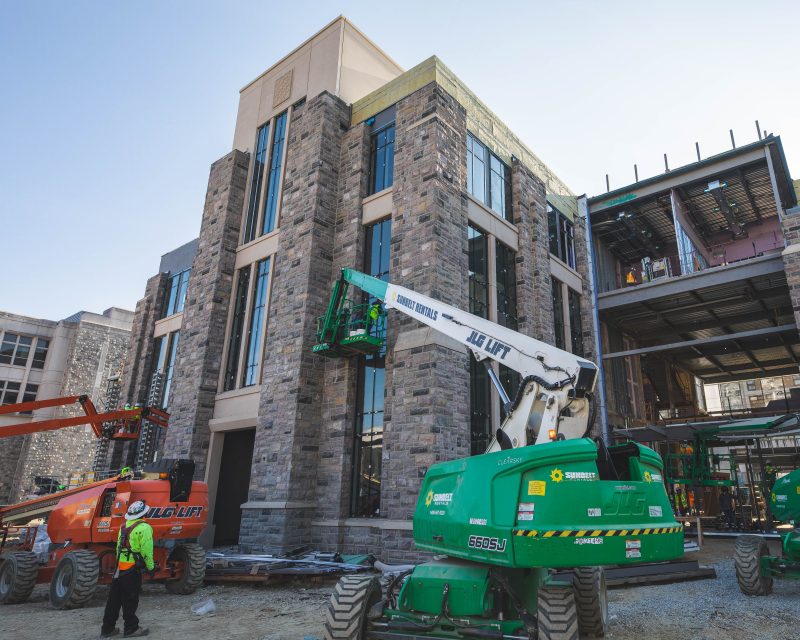 Grey Hokie Stone and glass Hitt Hall under construction surrounded by a green and an orange lift