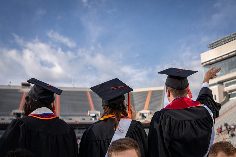 Three graduates wave during commencement ceremonies