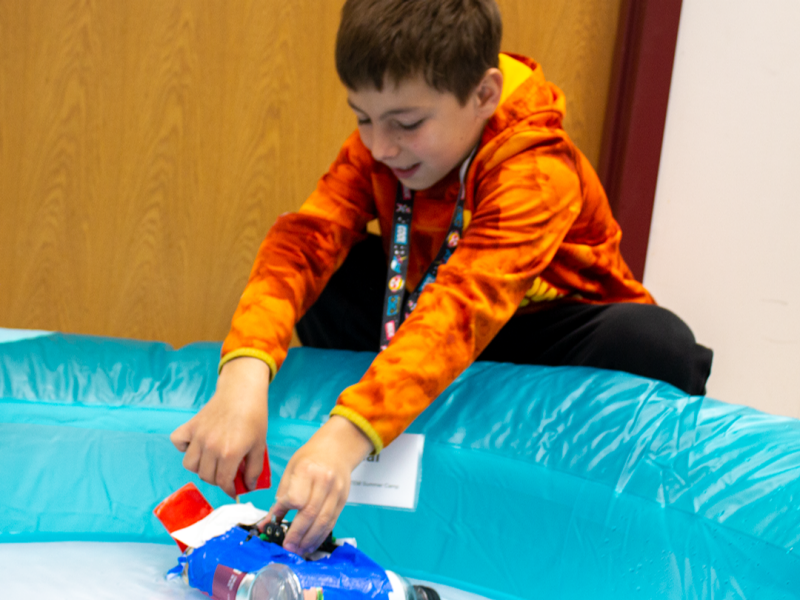 One boy playing with one of the activities in a plastic pool as part of the STEM summer camp.