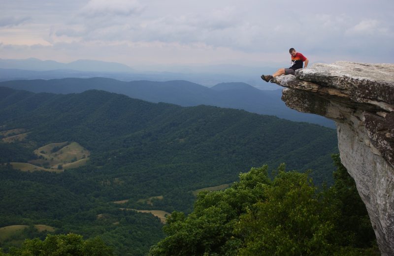 A student sitting on a rocky outcrop with views of the surrounding valley