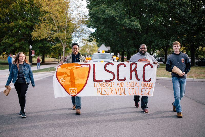 Members of the Leadership and Social Change Residential College march with banner in the 2019 Homecoming parade. 