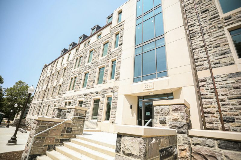 A modern collegiate gothic five story residence hall stands in bright sunlight.